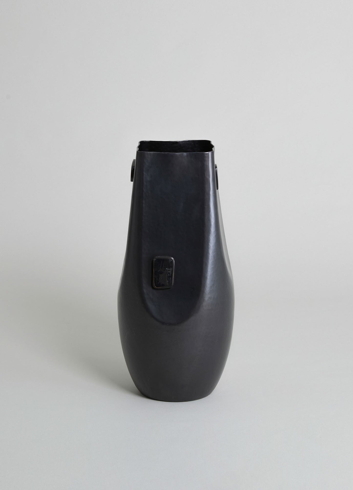 A tall, black ceramic vase with a smooth matte finish and a slightly tapered shape, set against a neutral background.