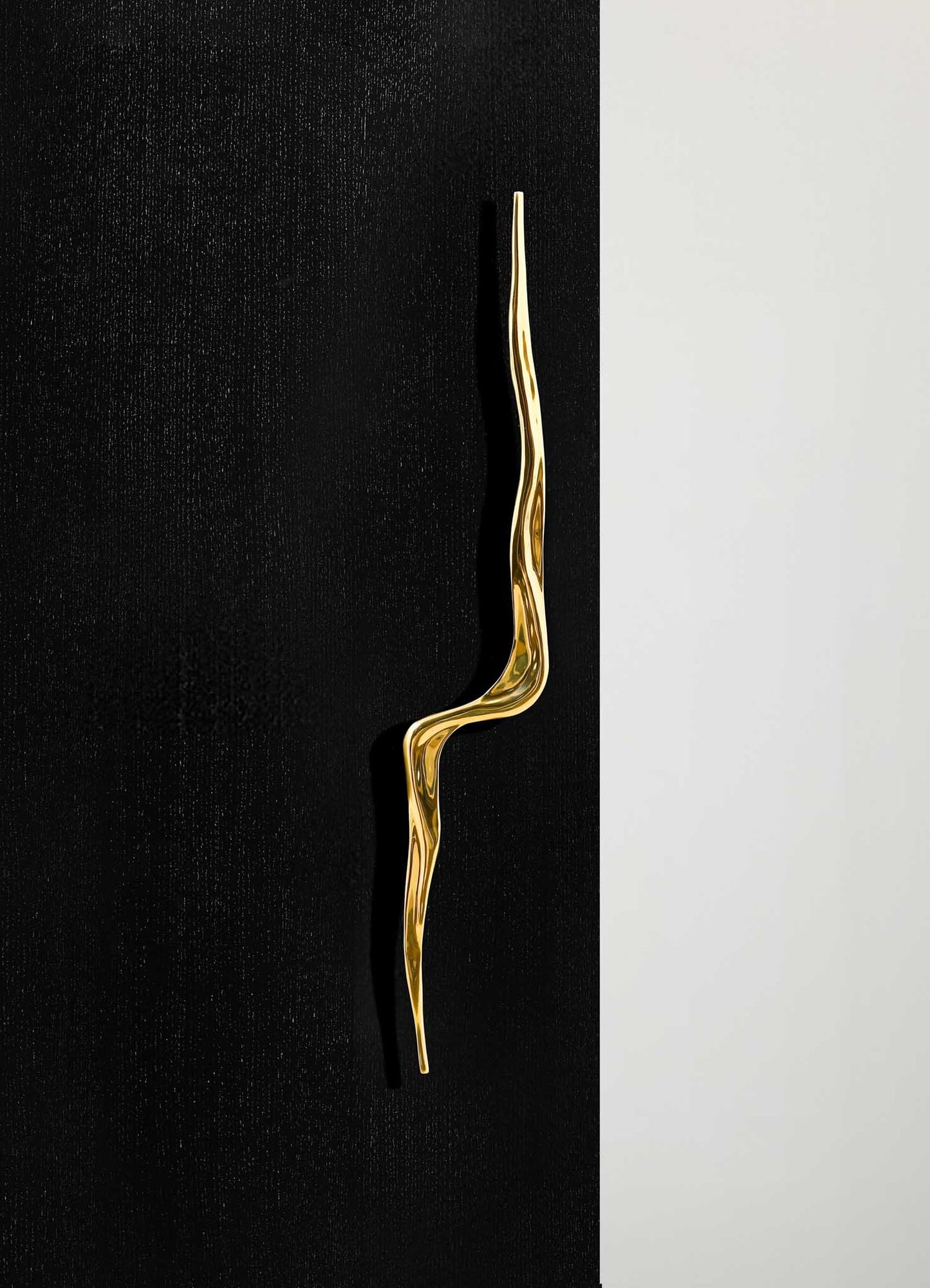 A gold-colored decorative object with a twisted, elongated shape set against a black textured background and a light gray surface.
