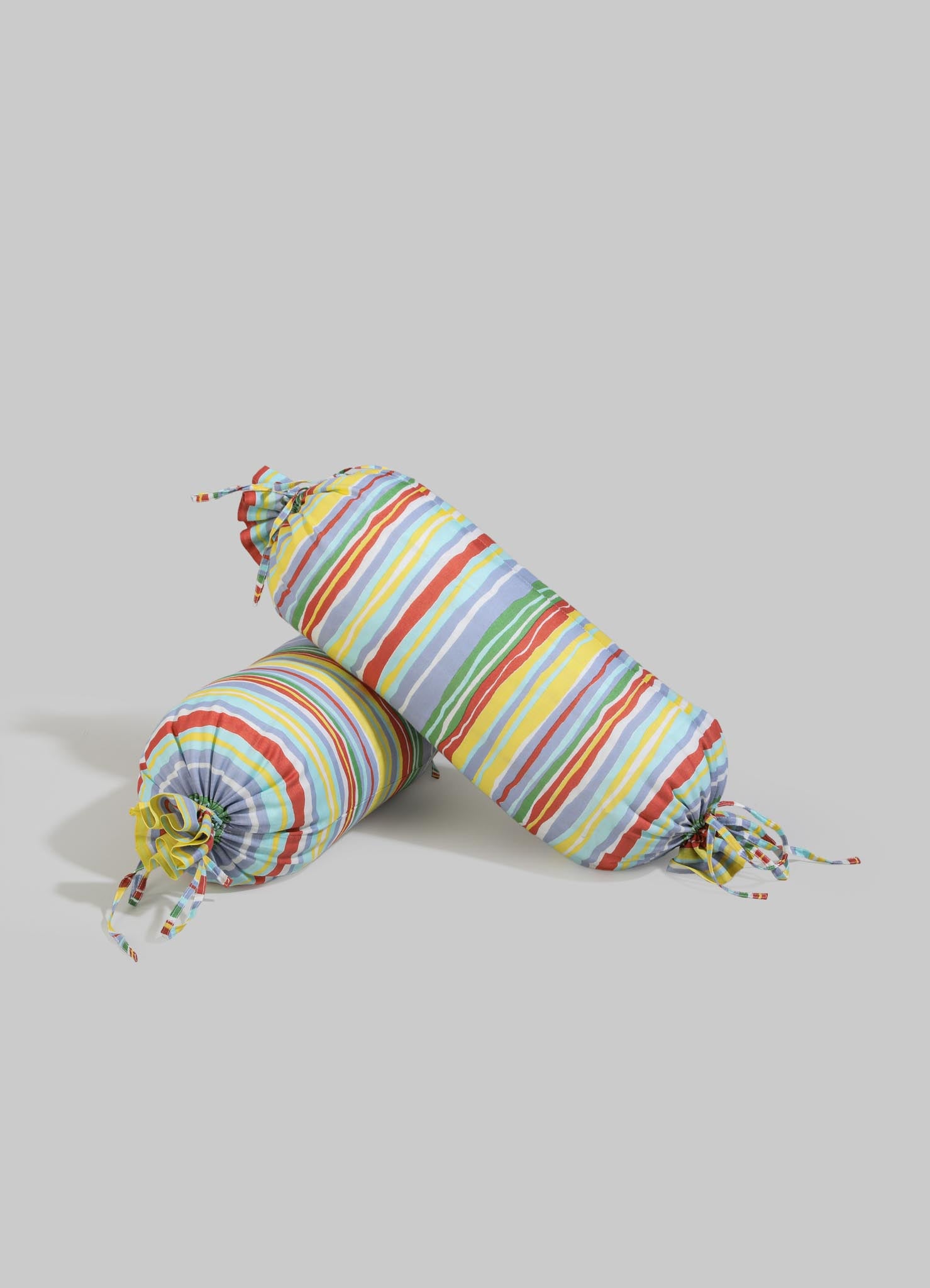 Striped fabric pillow and bolster cushions with multicolored horizontal lines in red, yellow, blue, green, and orange, made from lightweight textile material. The cushions feature knotted ends with matching fabric ties, creating a casual, colorful, and playful aesthetic.