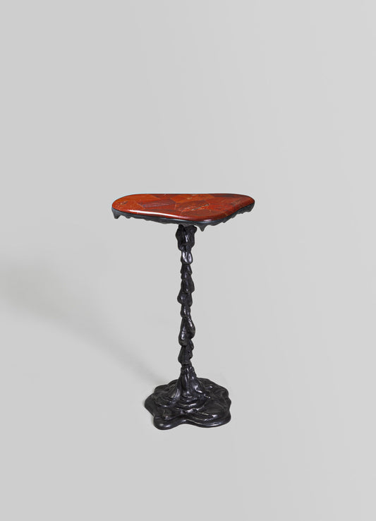 A sculptural side table with a reddish-orange marble top featuring a hexagonal pattern and a textured black metal base with an organic, irregular form.