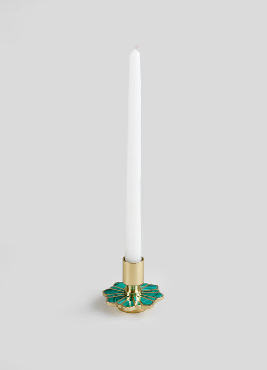 A tall white candle in a decorative brass candle holder with green enamel accents, featuring a geometric floral motif.