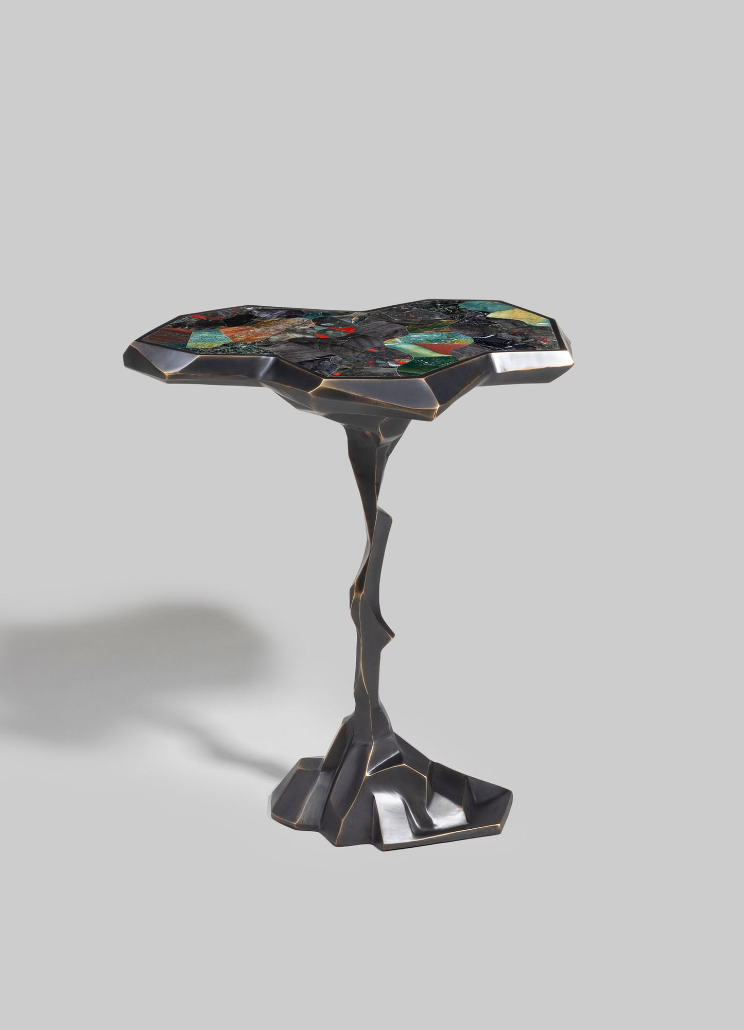 A decorative side table with an irregular-shaped tabletop made of colorful mosaic tiles in green, red, black, and blue tones, set on a sculptural black metal base with gold accents.