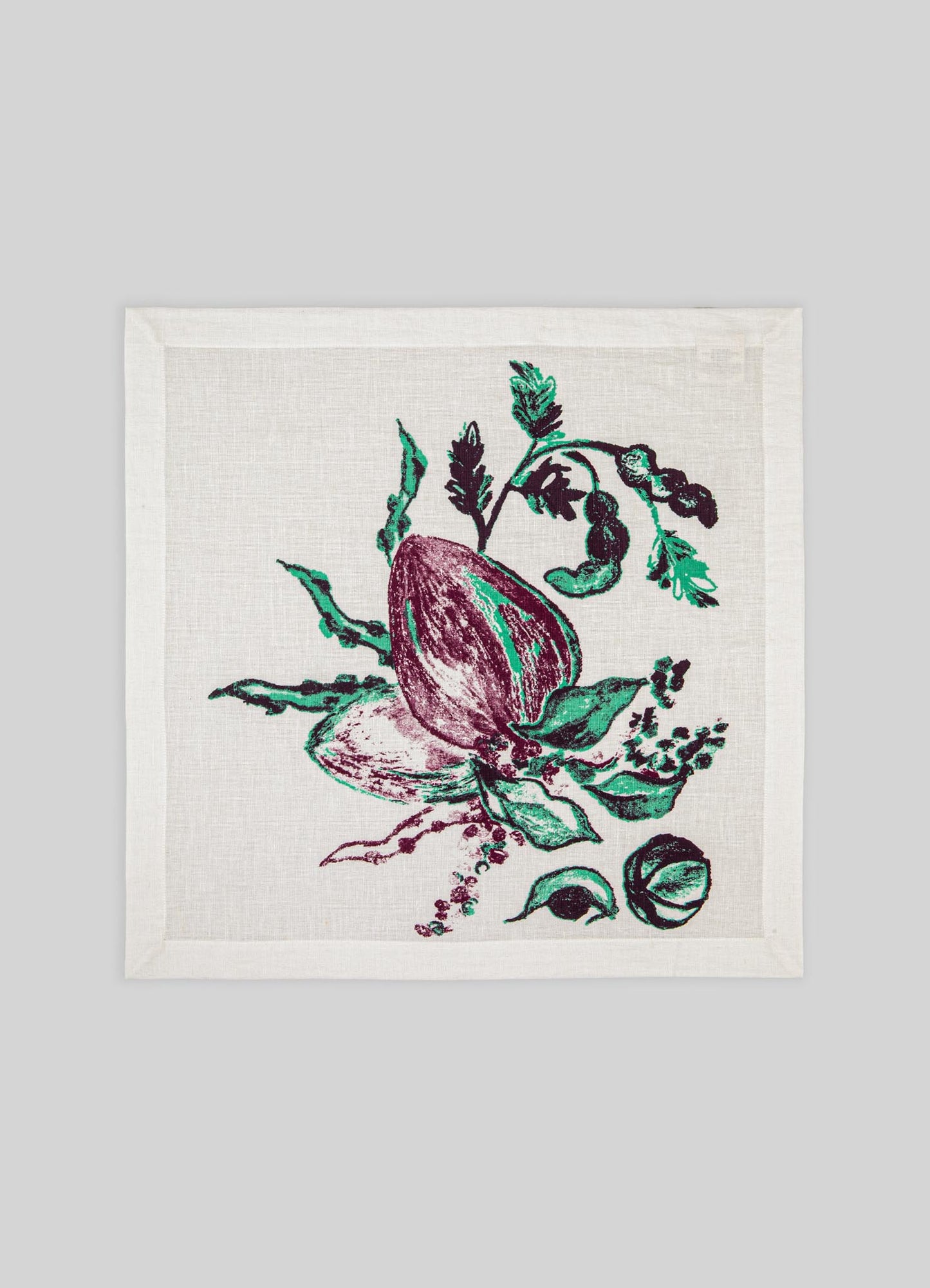 A cotton napkin with a botanical print featuring a purple and green fig fruit and leafy motifs, set against a neutral background. The design has a handcrafted, artistic style.
