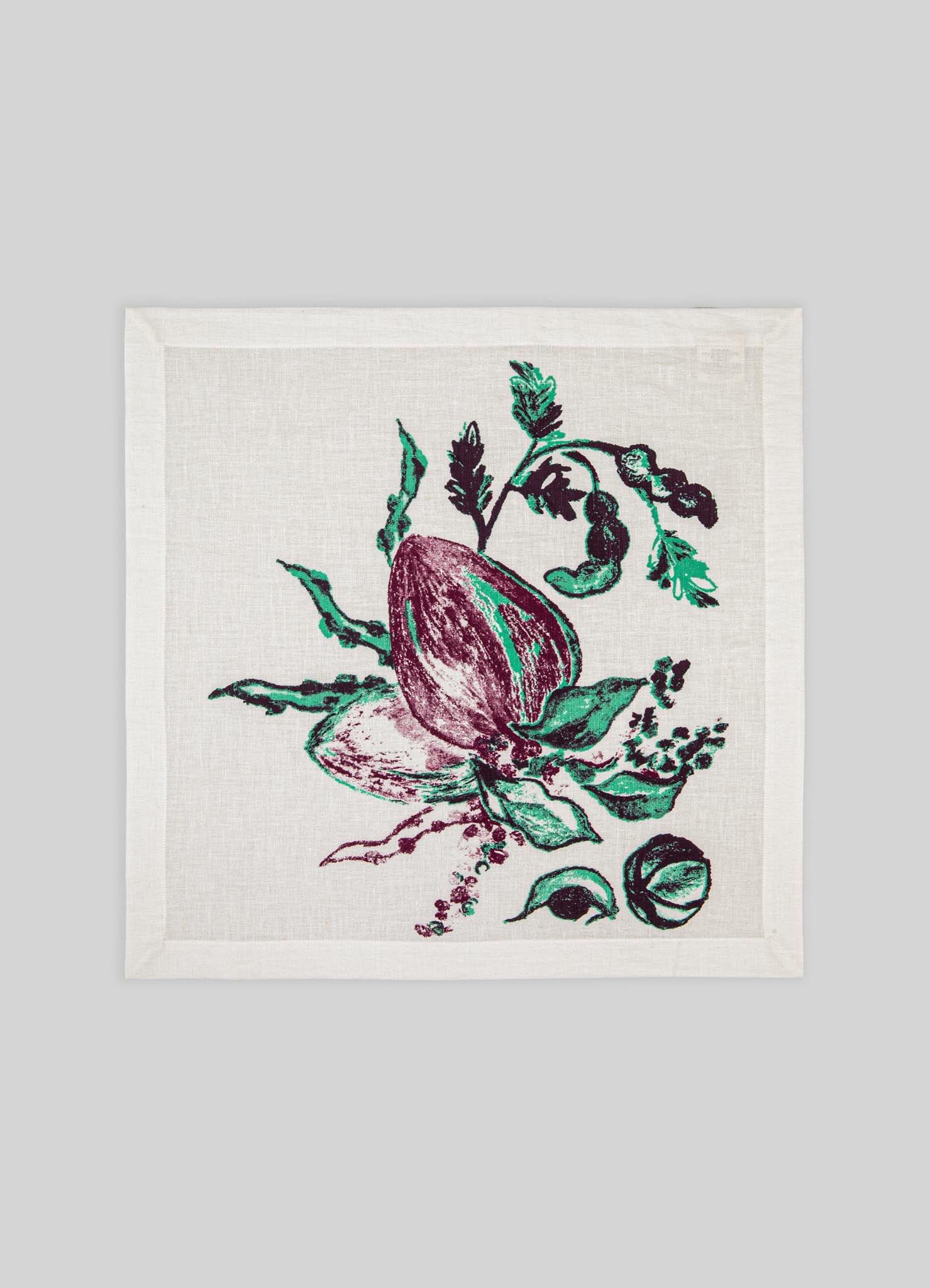A cotton napkin with a botanical print featuring a purple and green fig fruit and leafy motifs, set against a neutral background. The design has a handcrafted, artistic style.