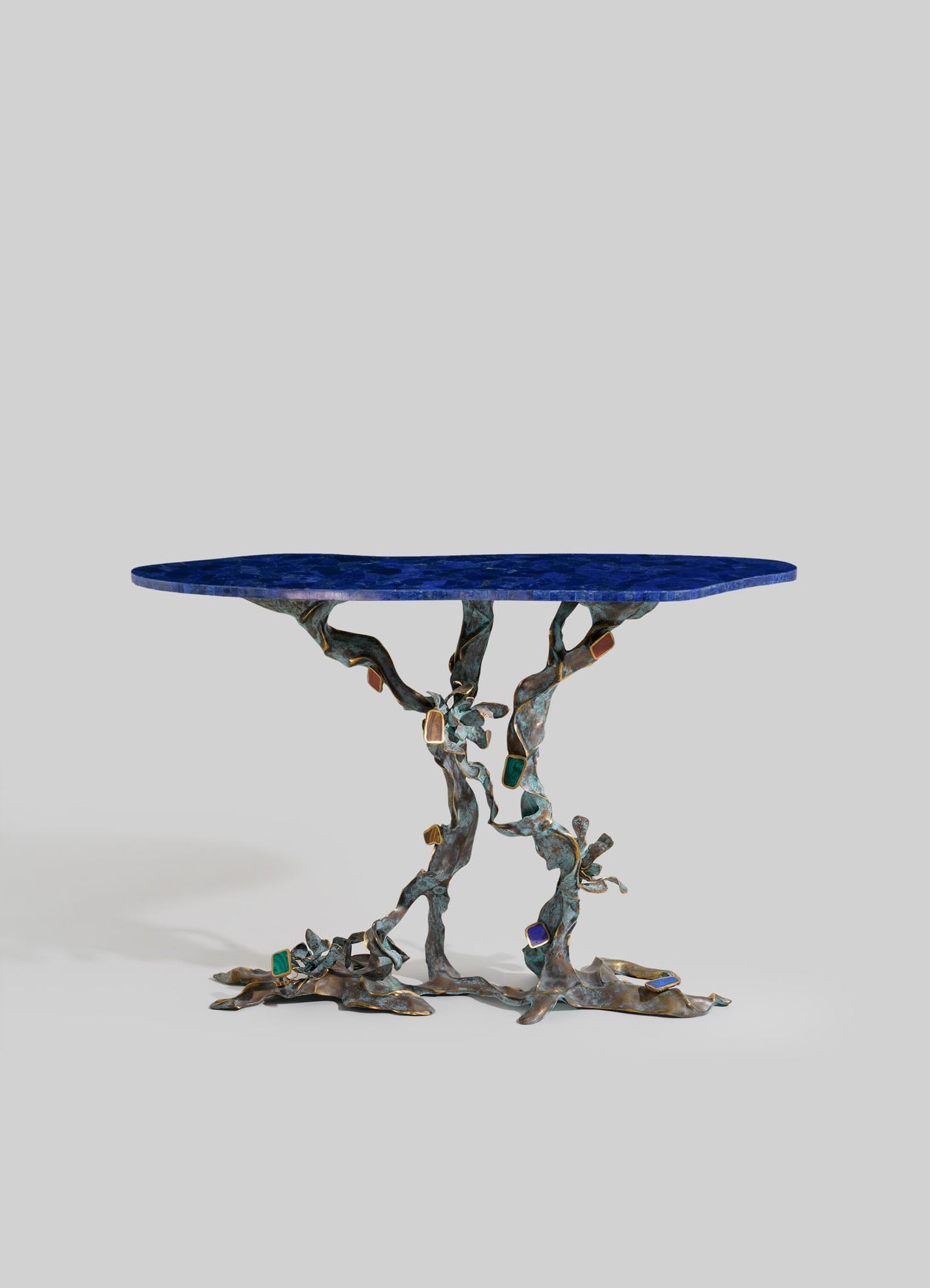 A decorative table with a textured cobalt blue marble top and an ornate bronze base featuring twisting, vine-like forms adorned with colorful rectangular inlays. The style appears contemporary with artistic and sculptural elements.