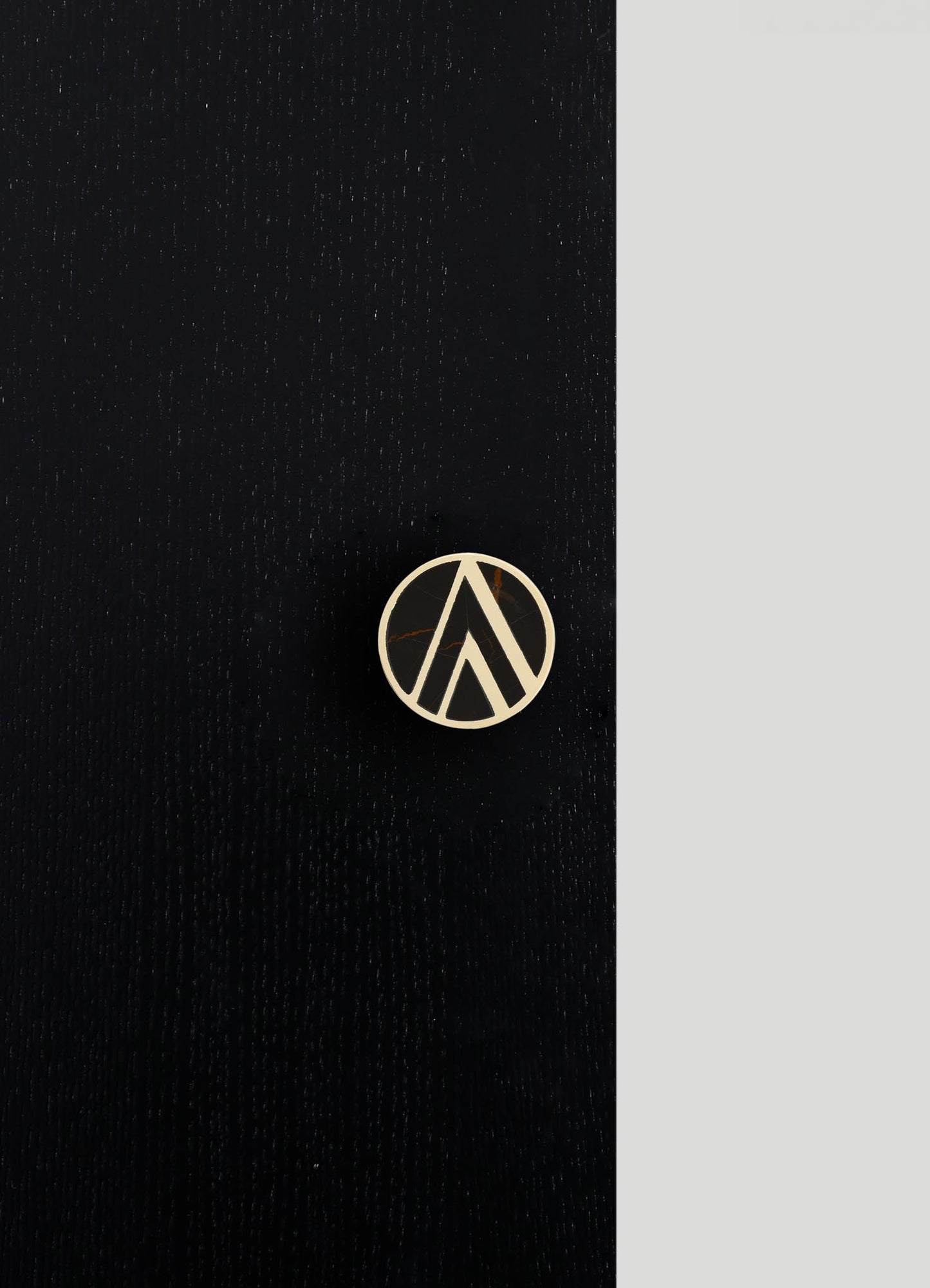 A round brooch with a black marble effect and gold-colored geometric lines, attached to black fabric with a subtle textured pattern.