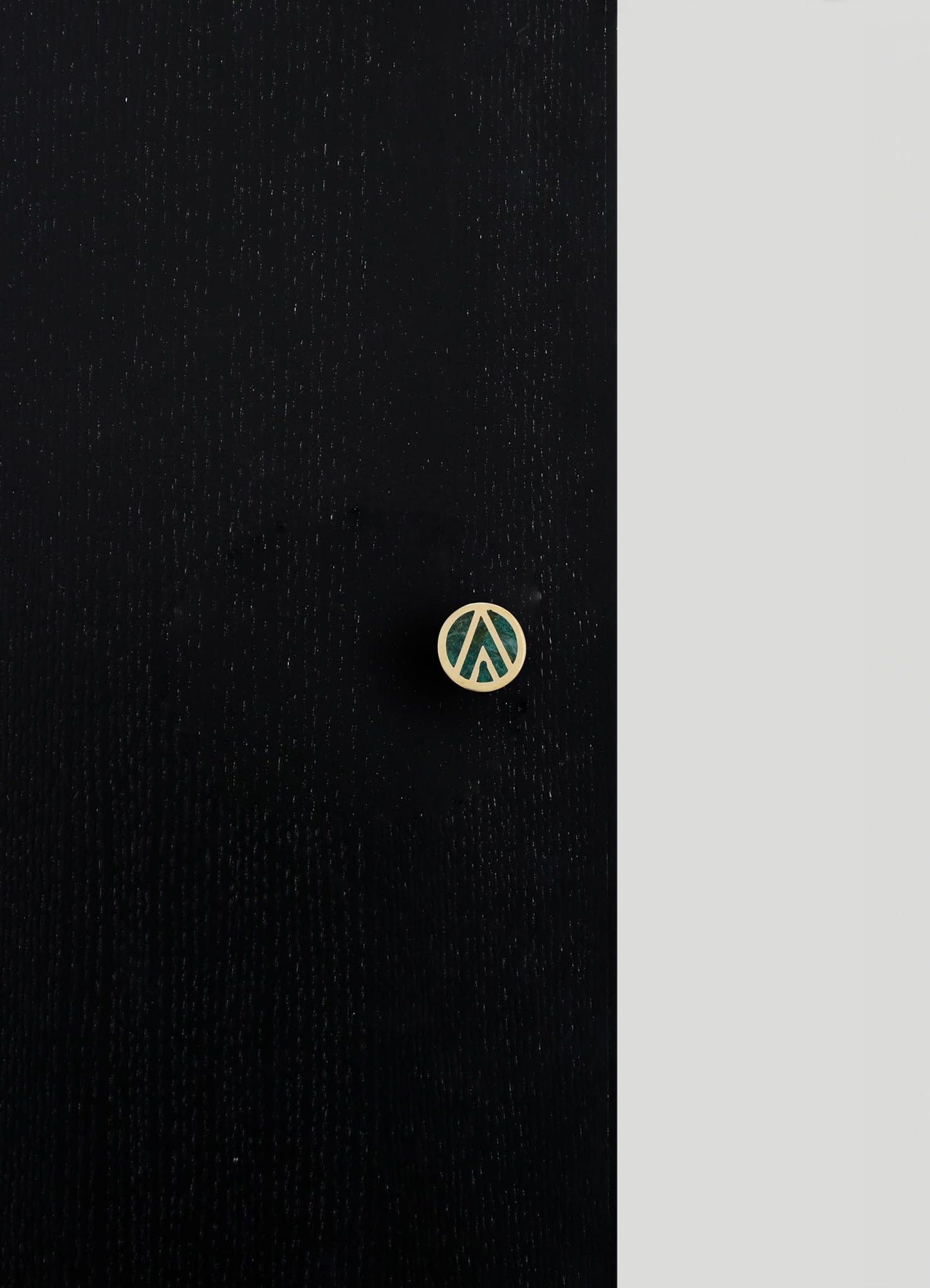 A black fabric garment with a subtle dotted pattern and a round gold-colored button featuring a stylized geometric cutout. The fabric appears textured and the design minimalist and modern.