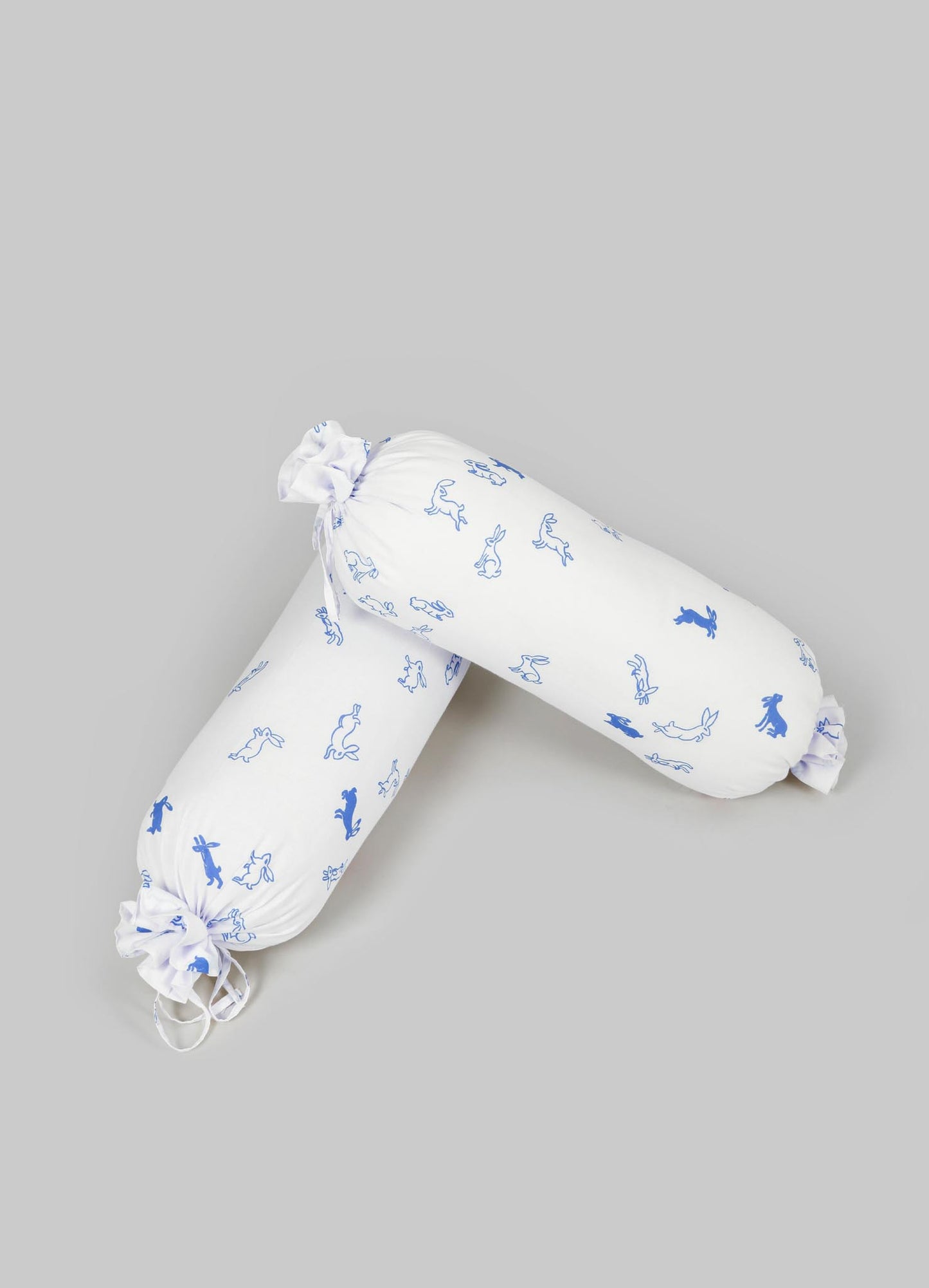 Rectangular cushion covers made of white fabric with a blue animal and botanical print, featuring drawstring ties at the ends. The design evokes a lightweight, playful style suitable for a cozy or casual setting.