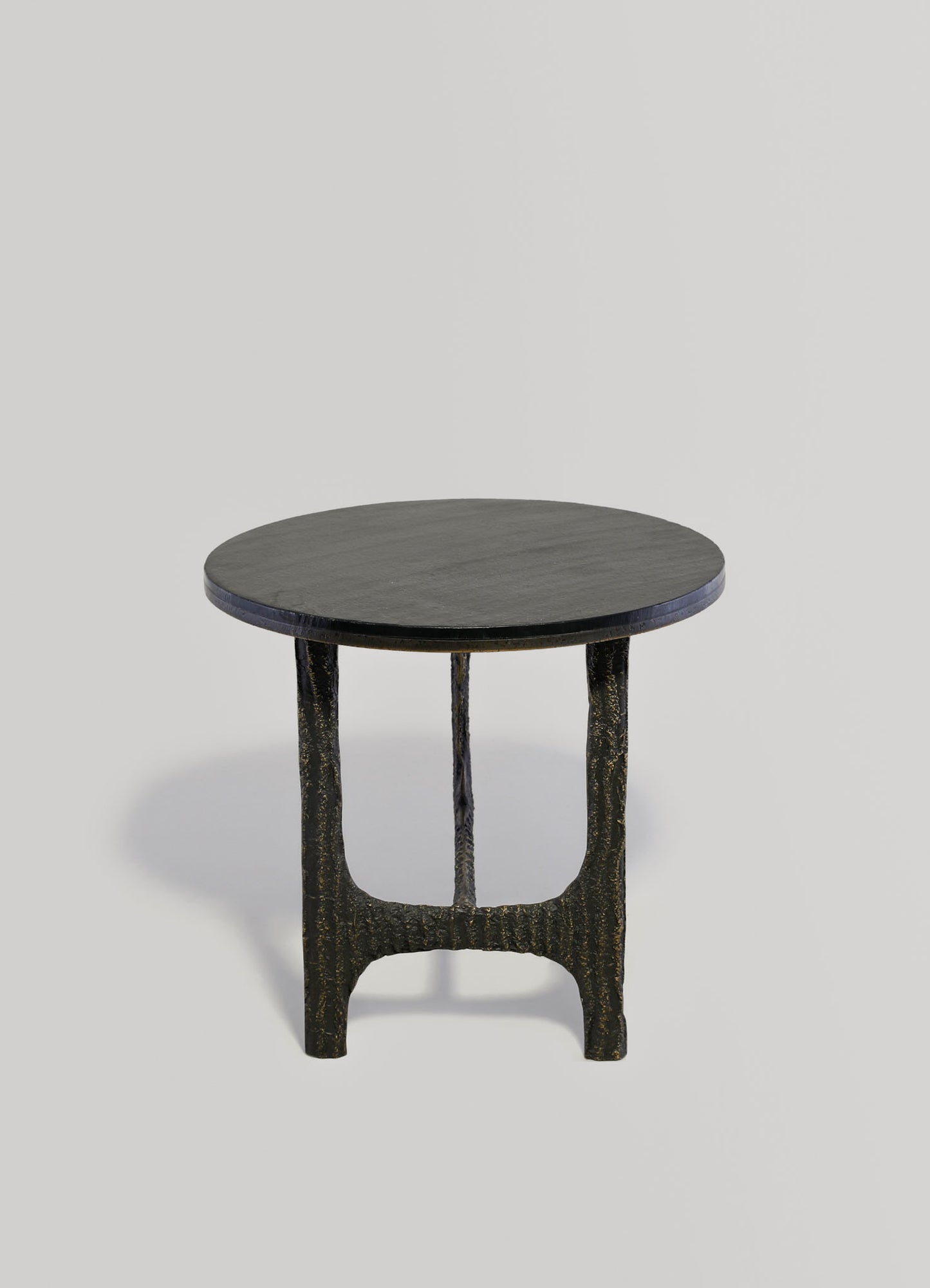 A small side table with a round dark wood top and sculptural black and gold finished legs, featuring a contemporary design with textured, irregular surfaces.