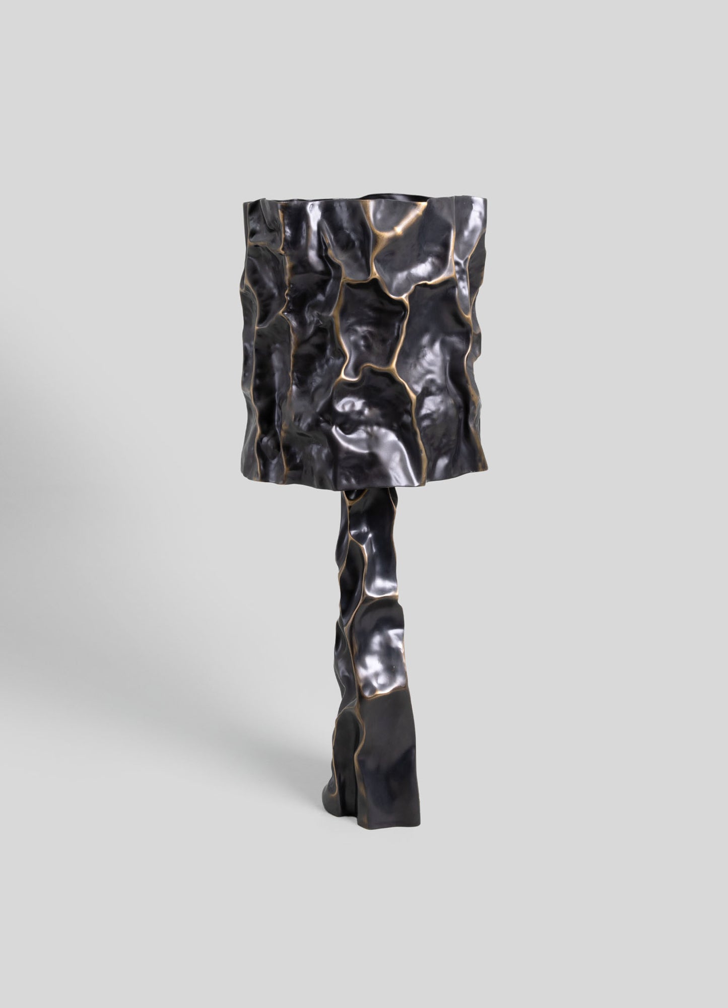 A sculptural table lamp with a textured, abstract design in black and metallic gold accents, featuring a standing base and a rectangular lampshade with a crumpled, organic surface.