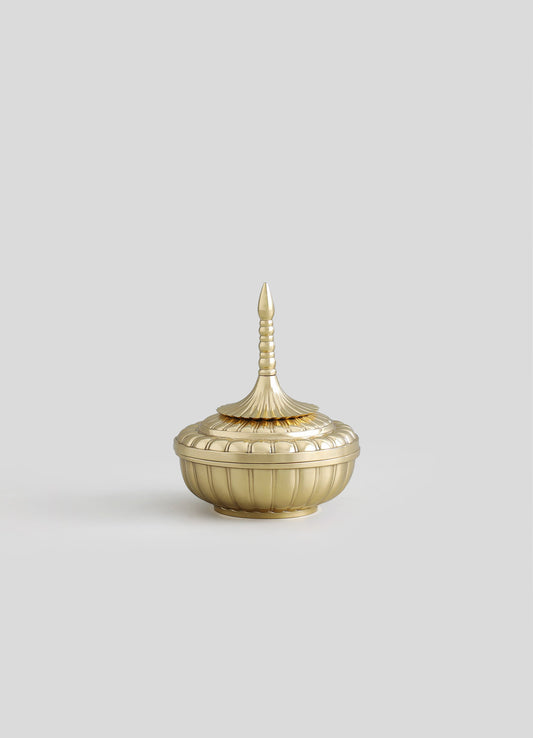 A decorative bowl with a lid made of metallic gold-colored material, featuring a fluted design and a pointed finial on top. The piece has a vintage or ornate style with detailed ridges and a rounded base.