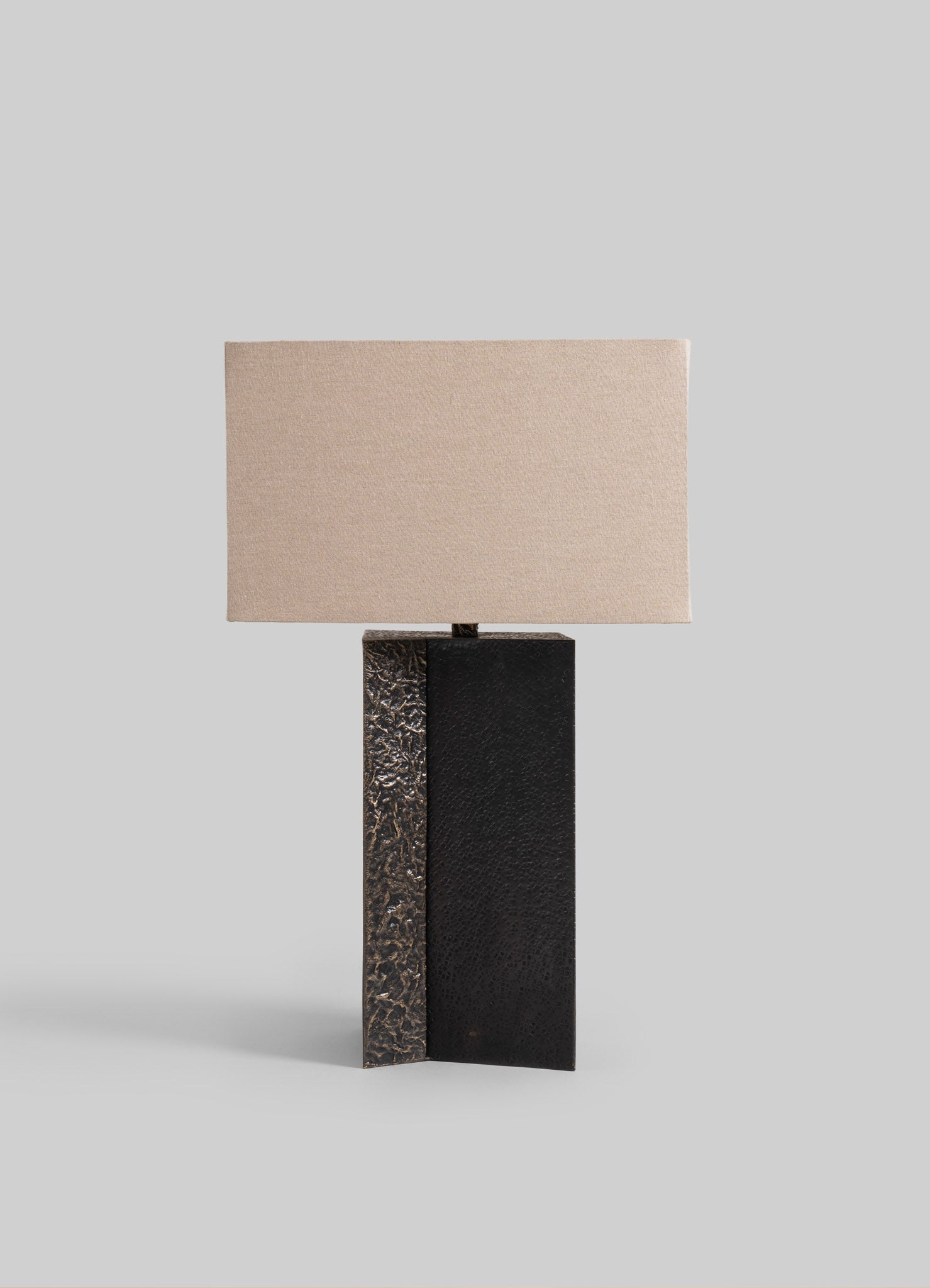 A table lamp featuring a textured black and metallic bronze base with a rectangular beige fabric shade, presenting a contemporary and minimalist design.