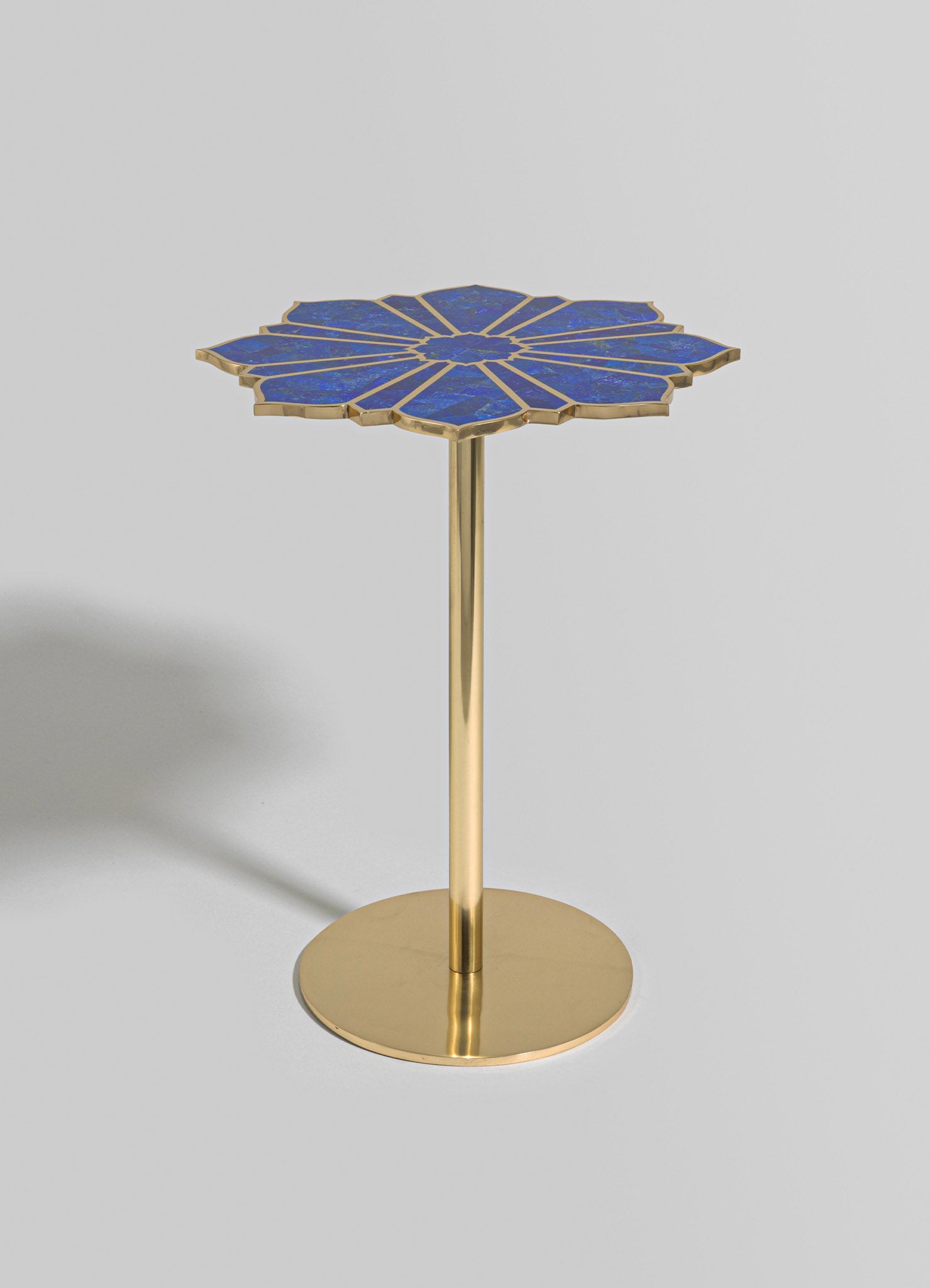 A side table with a geometric-flower shaped top featuring blue terrazzo with gold trim, supported by a slender gold metal pedestal on a round base.