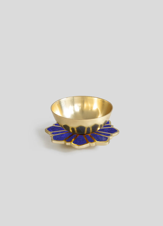 A decorative bowl with a polished gold interior and exterior, placed on a blue and gold floral-shaped base with geometric elements.