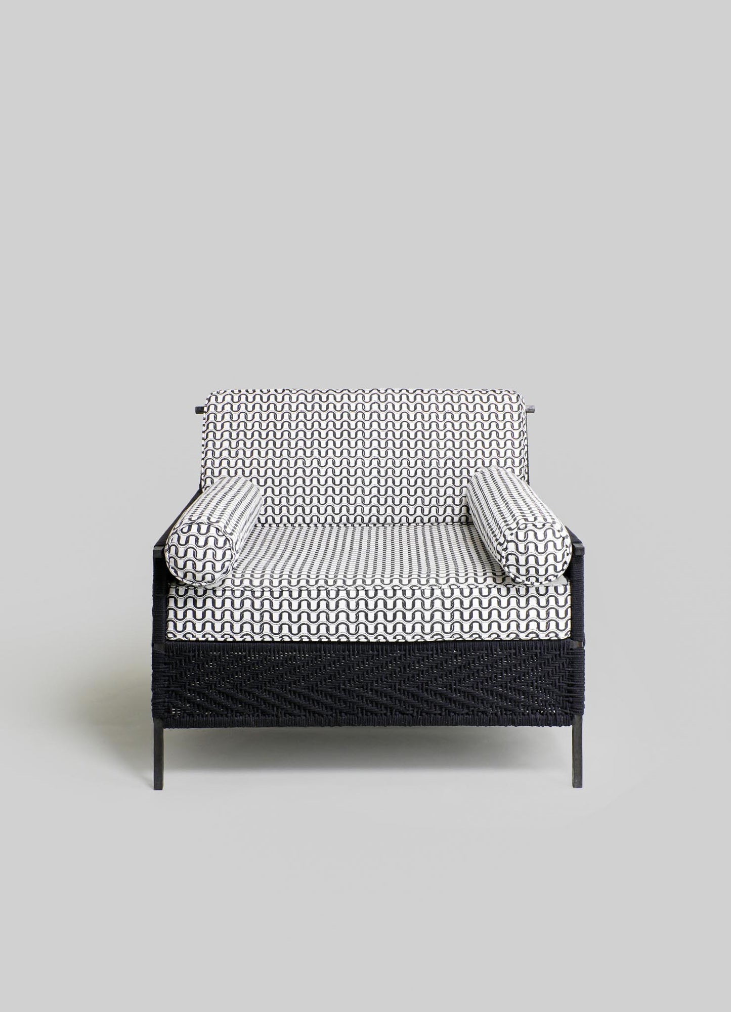 Wicker loveseat with a black frame and fabric cushions featuring a black and white geometric wavy pattern. The cushions include two bolster pillows with the same pattern, set against a neutral gray background.