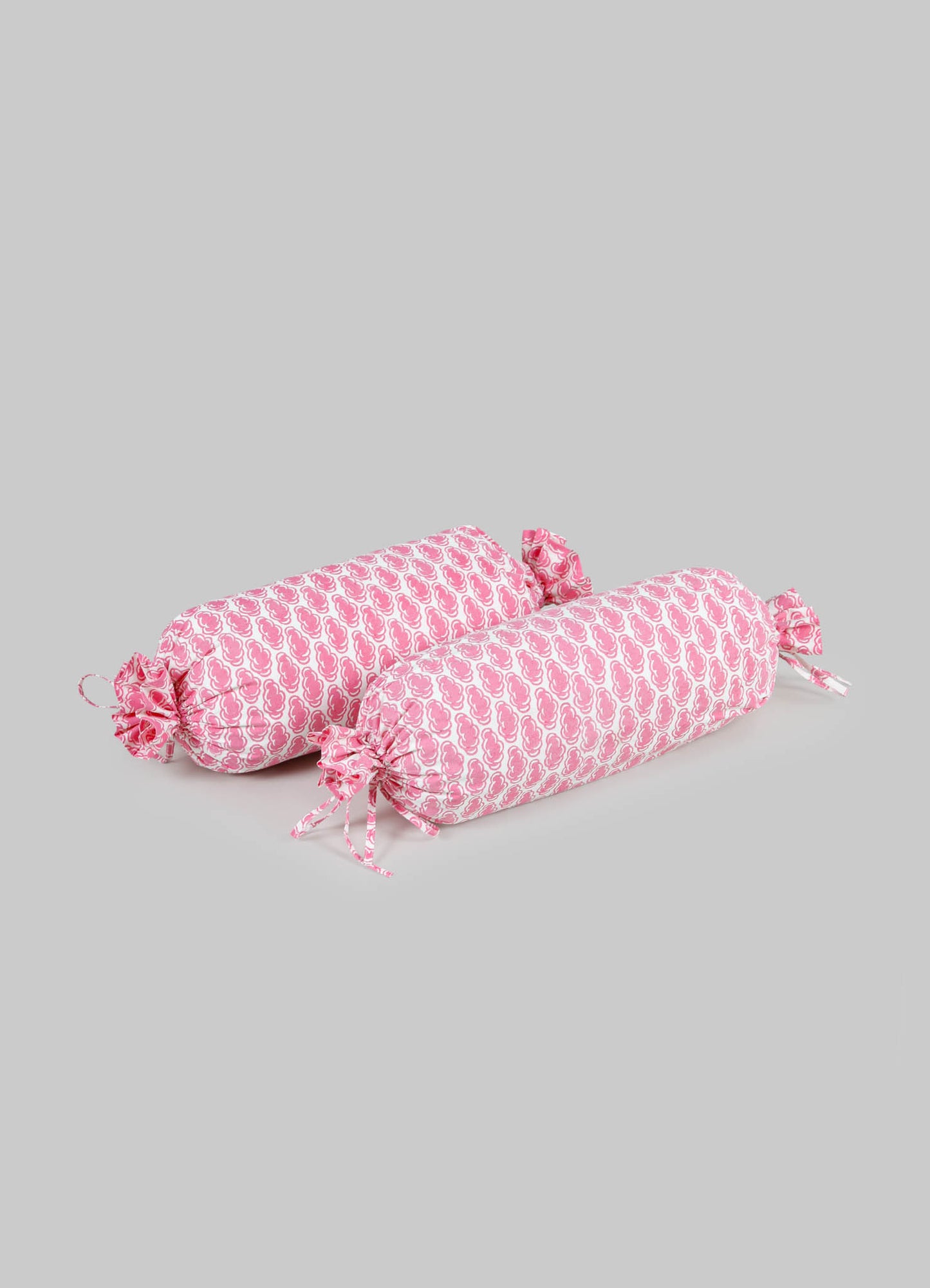 Pair of cylindrical bolster cushions with pink and white floral pattern fabric and ruffled ties, designed for decorative or seating use.