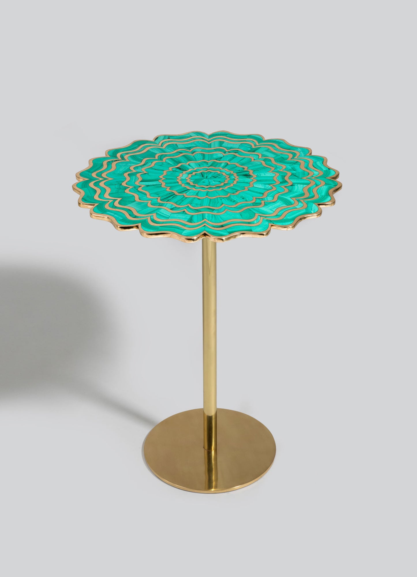 A decorative side table with a round, scalloped top featuring a turquoise and gold geometric pattern, supported by a slender gold metal stem and a circular gold base. The style appears contemporary with a vibrant, artistic motif.
