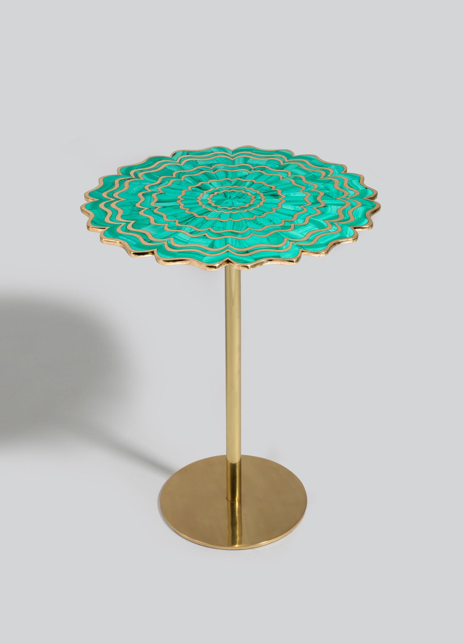 A decorative side table with a round, scalloped top featuring a turquoise and gold geometric pattern, supported by a slender gold metal stem and a circular gold base. The style appears contemporary with a vibrant, artistic motif.