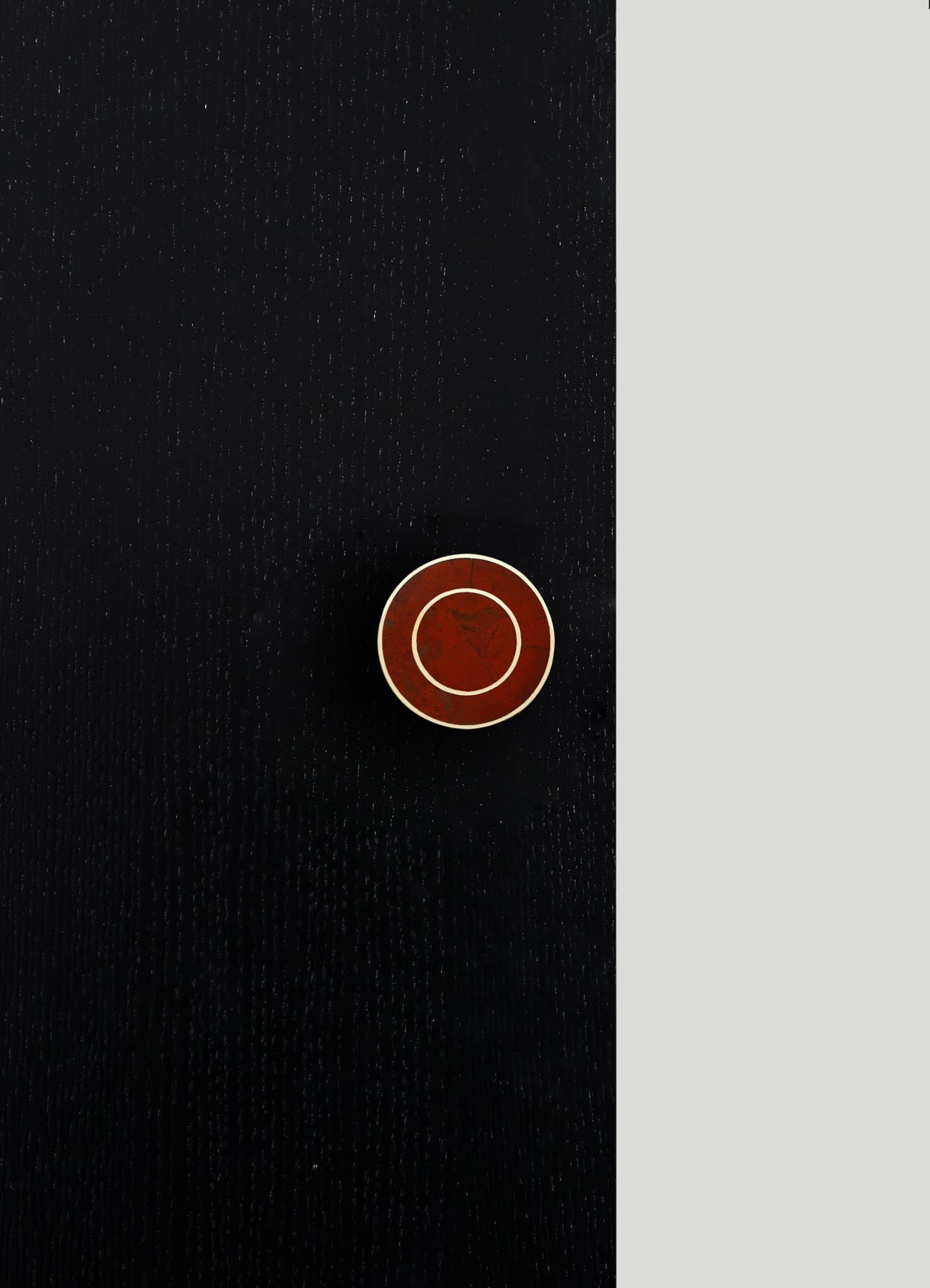 A black leather surface with a textured pattern and a round, reddish-brown button with a metallic ring in the center. The background includes a light gray area contrasting with the leather surface.