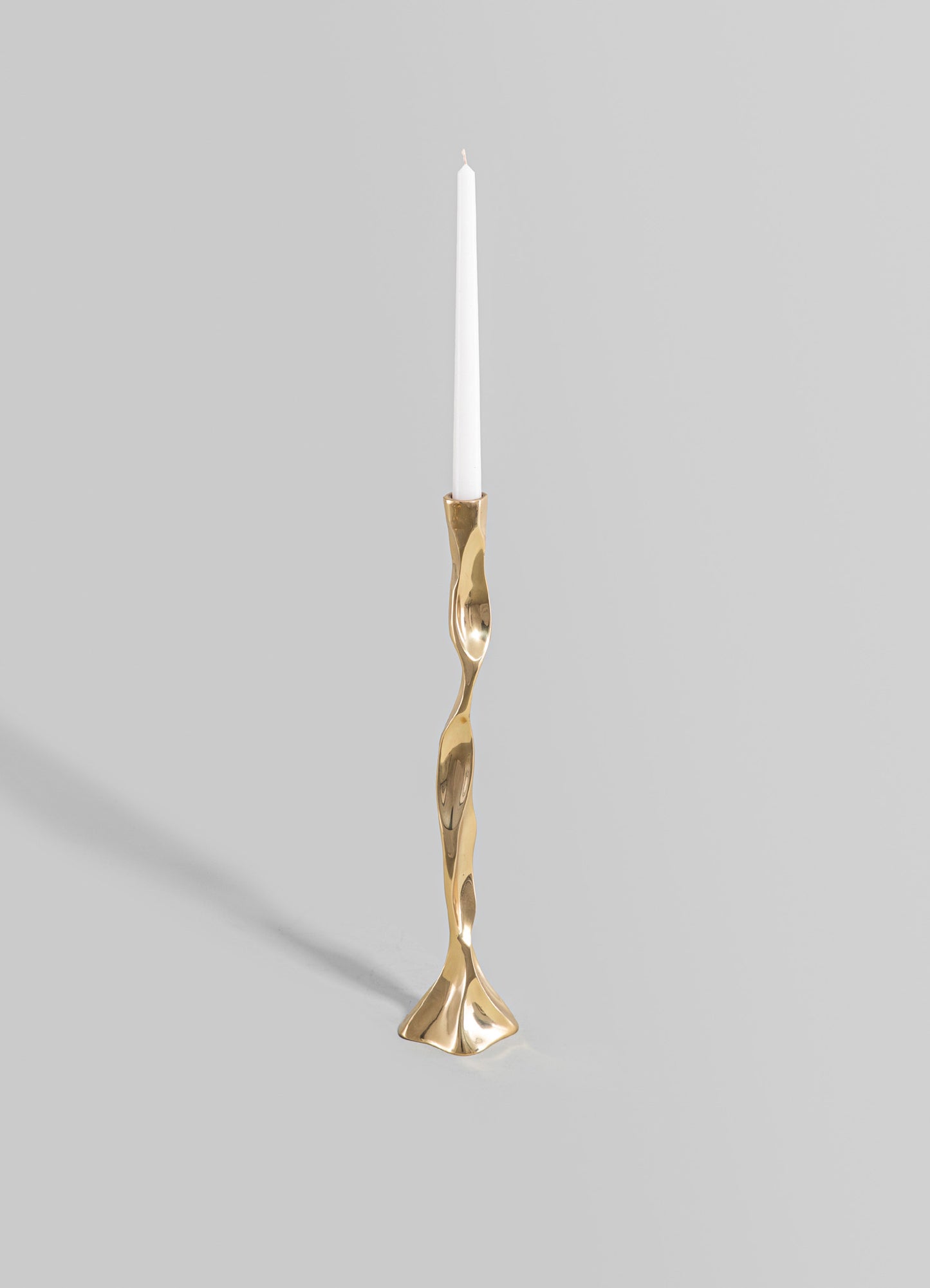A sculptural brass candlestick with an irregular, wavy design and a polished gold finish, holding a tall white taper candle.
