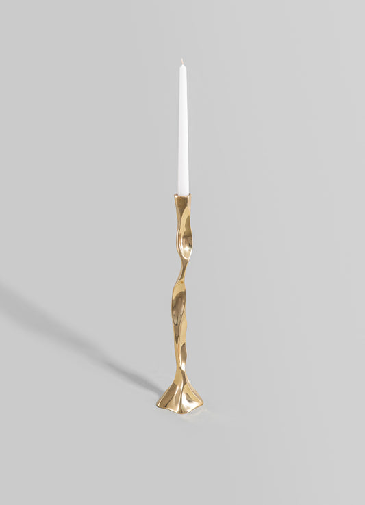 A sculptural brass candlestick with an irregular, wavy design and a polished gold finish, holding a tall white taper candle.