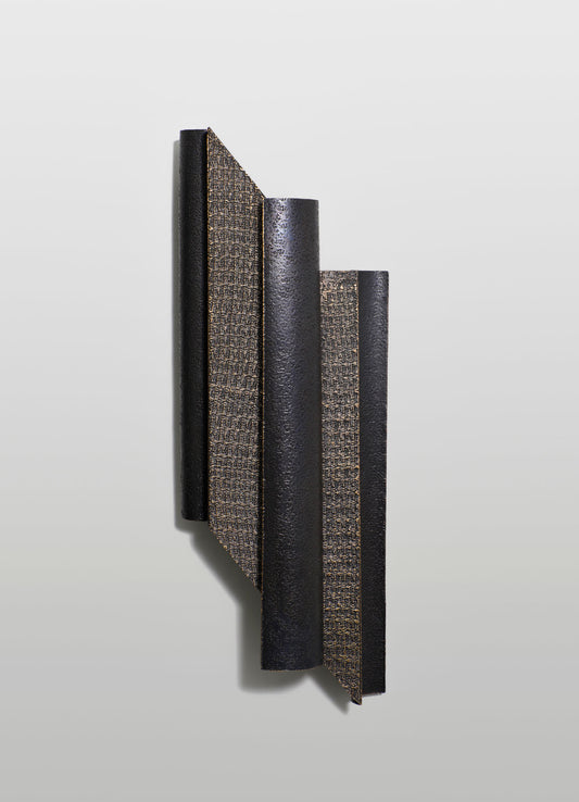 A set of four cylindrical and rectangular decorative objects with textured surfaces in black and gold tones, mounted on a light background. The design features contrasting materials and finishes, emphasizing a modern, minimalist style.