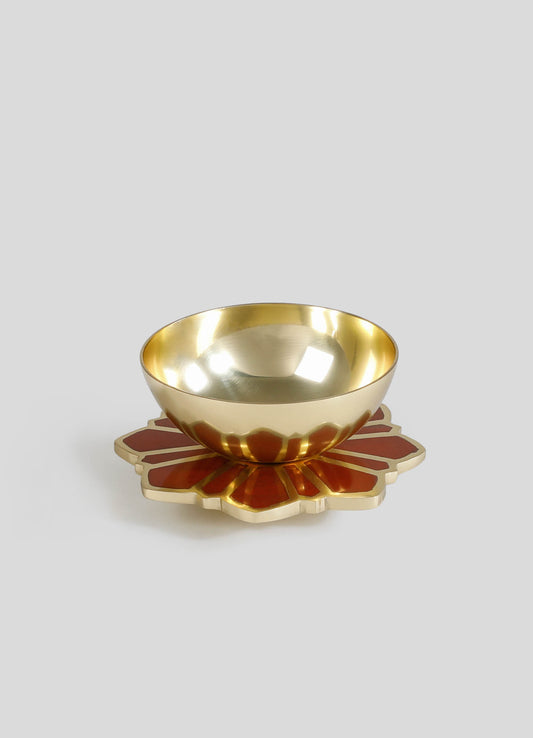 A decorative brass bowl with a polished, reflective surface, accompanied by a flower-shaped ceramic coaster with a red and beige pattern.