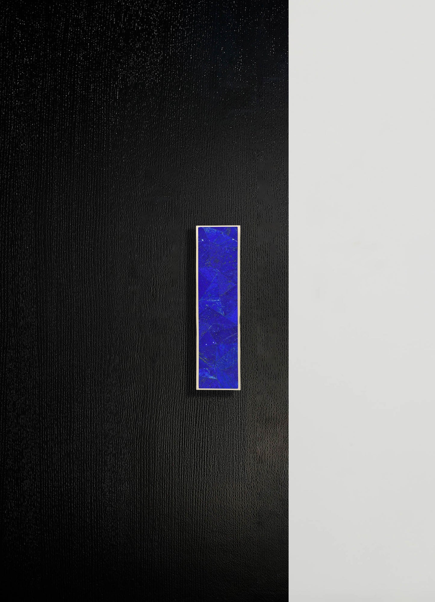 A wall light fixture featuring a rectangular blue glass shade with a textured, marbled pattern, mounted on a contrasting black and white wall. The fixture has a minimalist, contemporary style with a sleek metal frame surrounding the glass.