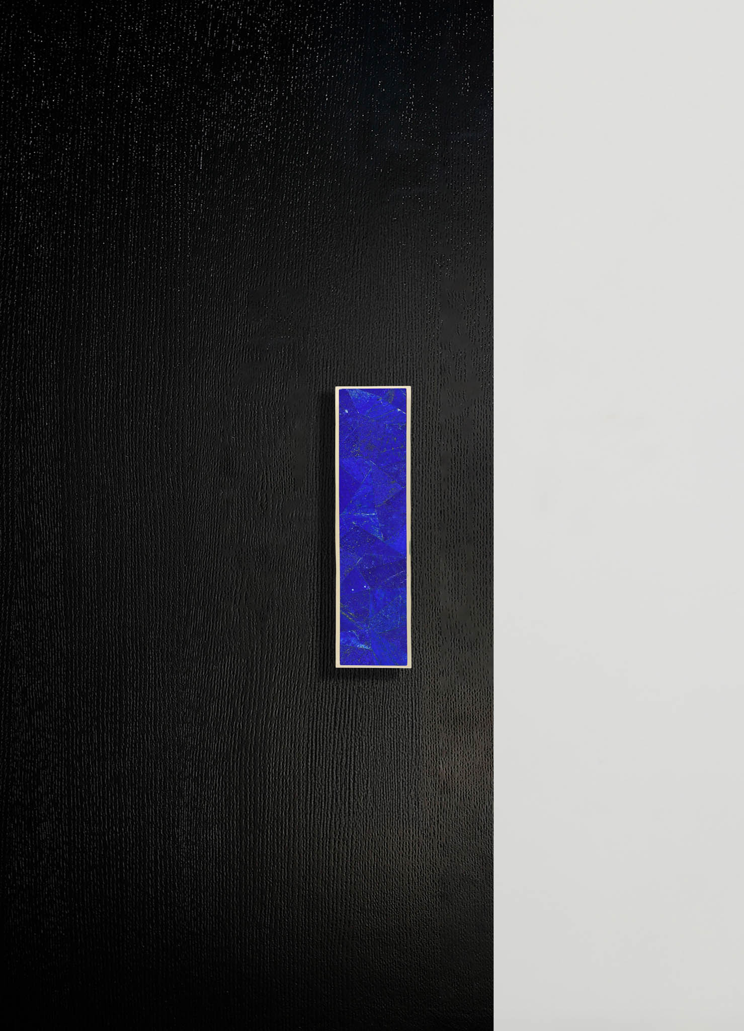 A wall light fixture featuring a rectangular blue glass shade with a textured, marbled pattern, mounted on a contrasting black and white wall. The fixture has a minimalist, contemporary style with a sleek metal frame surrounding the glass.