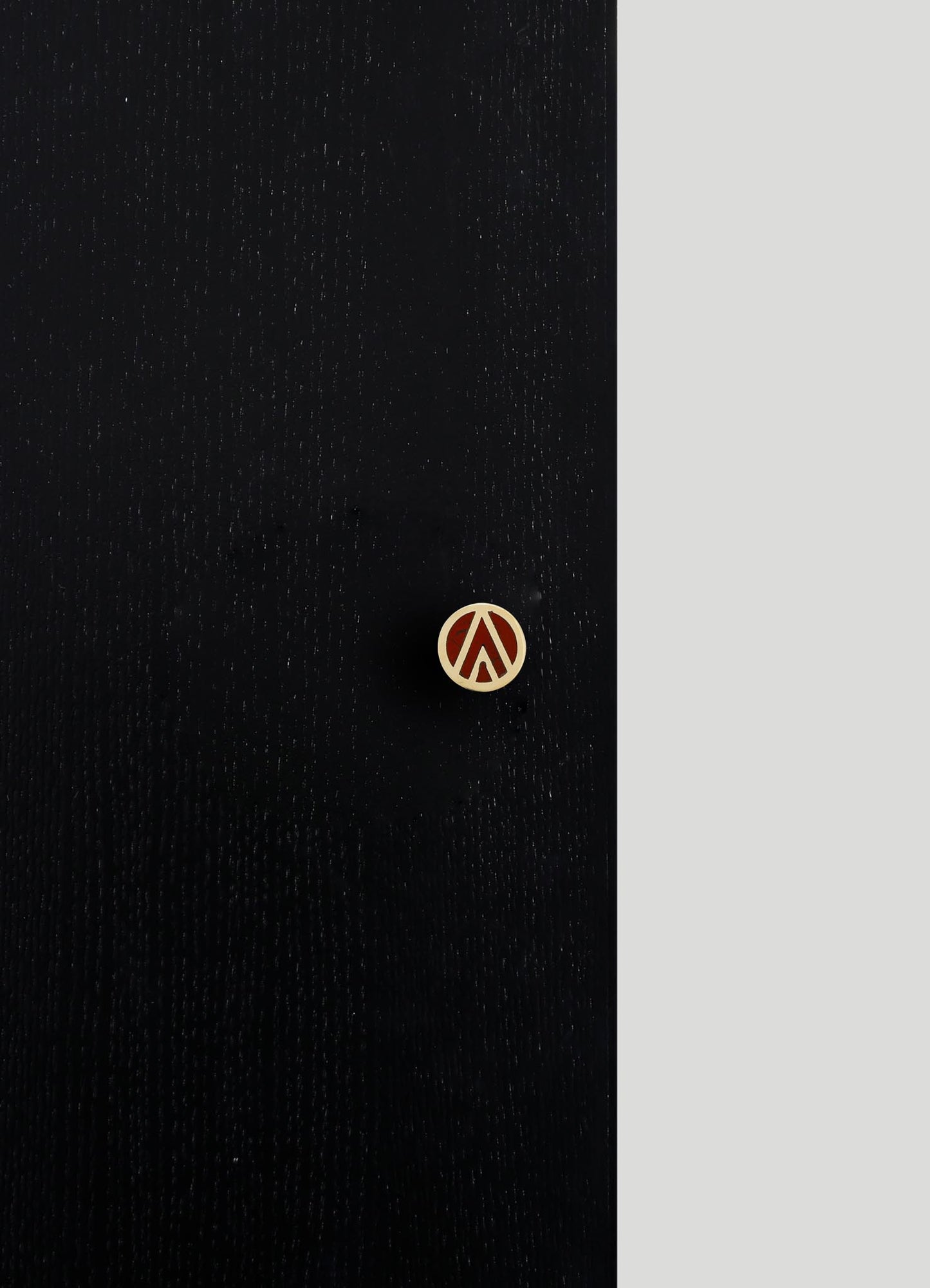 Black fabric with a subtle dotted texture and a small circular button featuring a geometric cutout in gold. The background includes a contrasting light gray area, emphasizing the fabric's material and the decorative button.
