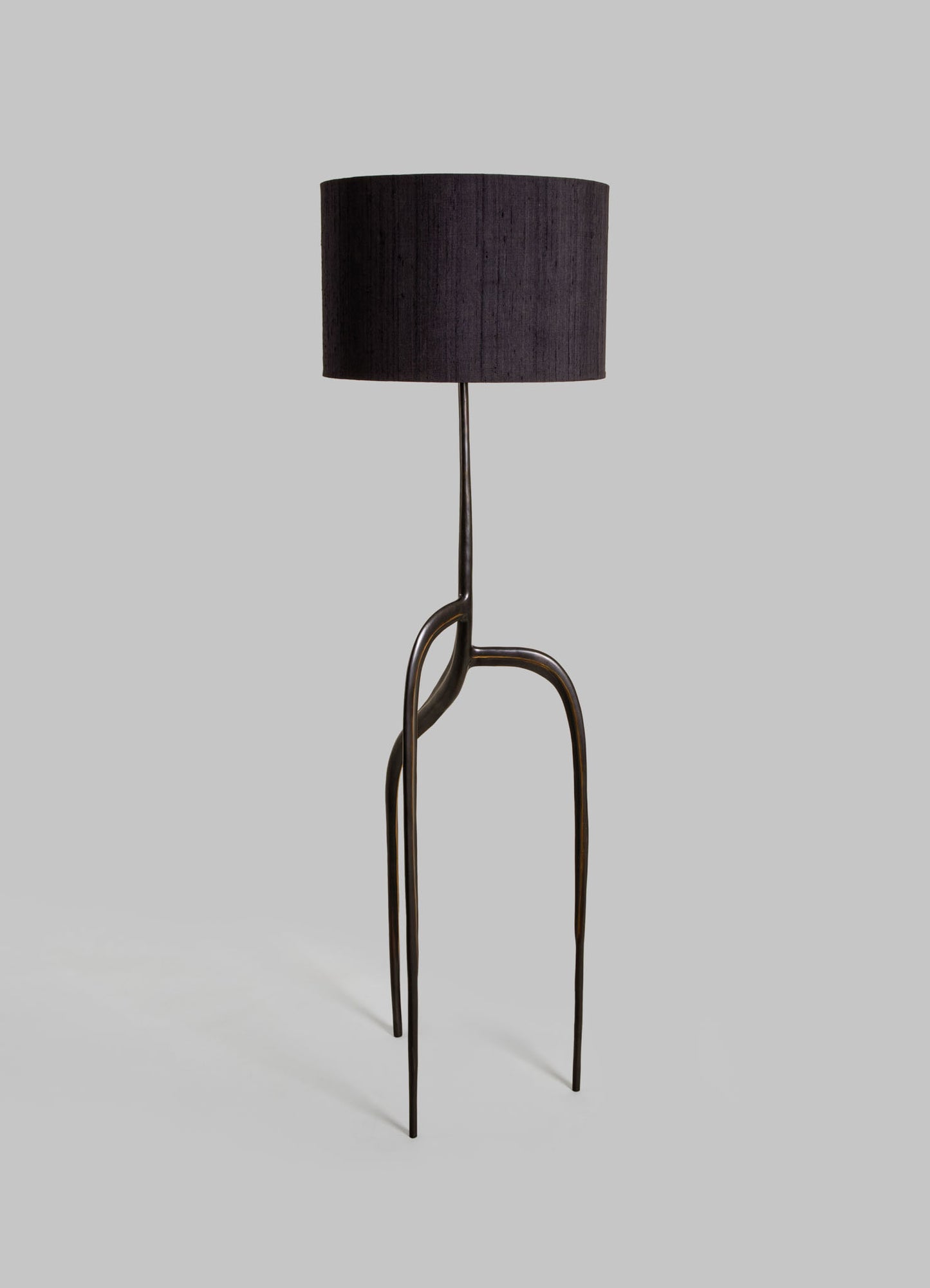 A floor lamp with a black fabric drum lampshade and a sculptural metal base featuring curved, elongated legs in a dark finish, creating a contemporary and artistic look.