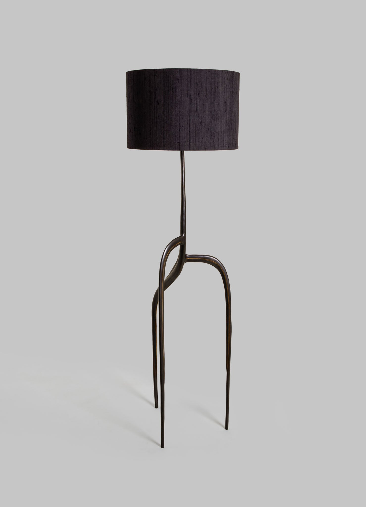 A floor lamp with a black fabric drum lampshade and a sculptural metal base featuring curved, elongated legs in a dark finish, creating a contemporary and artistic look.