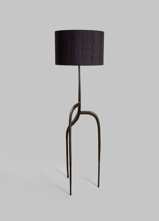 A floor lamp with a black fabric drum lampshade and a sculptural metal base featuring curved, elongated legs in a dark finish, creating a contemporary and artistic look.