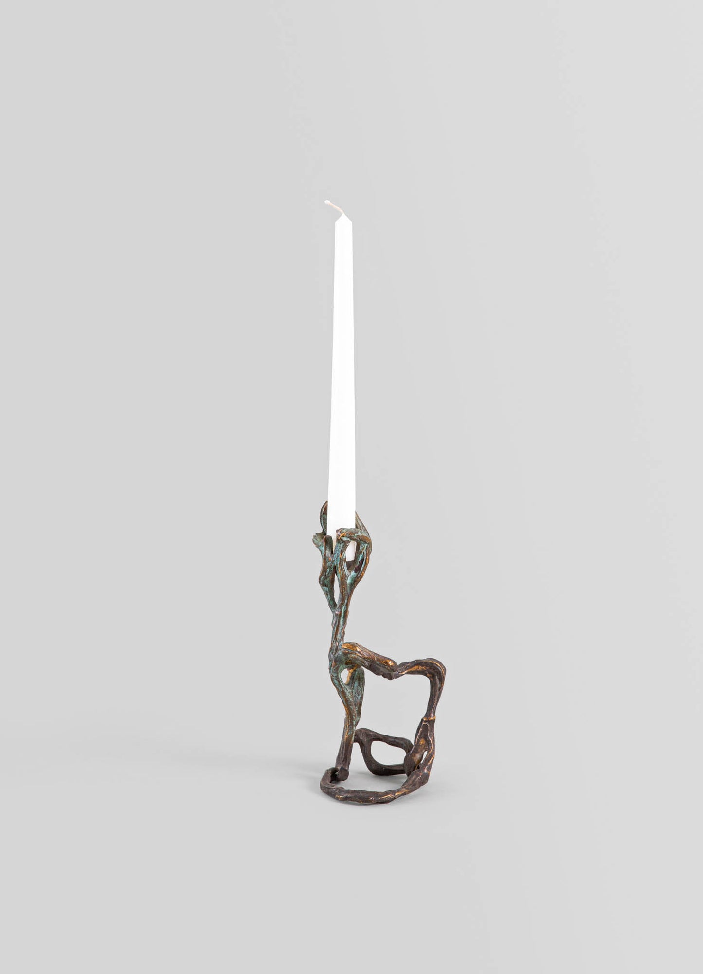 Brass candlestick with an organic, twisted design resembling natural branches, holding a tall, white tapered candle, set against a neutral background.