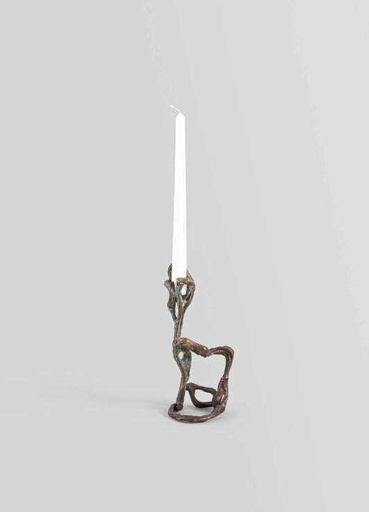 Brass candlestick with an organic, twisted design resembling natural branches, holding a tall, white tapered candle, set against a neutral background.