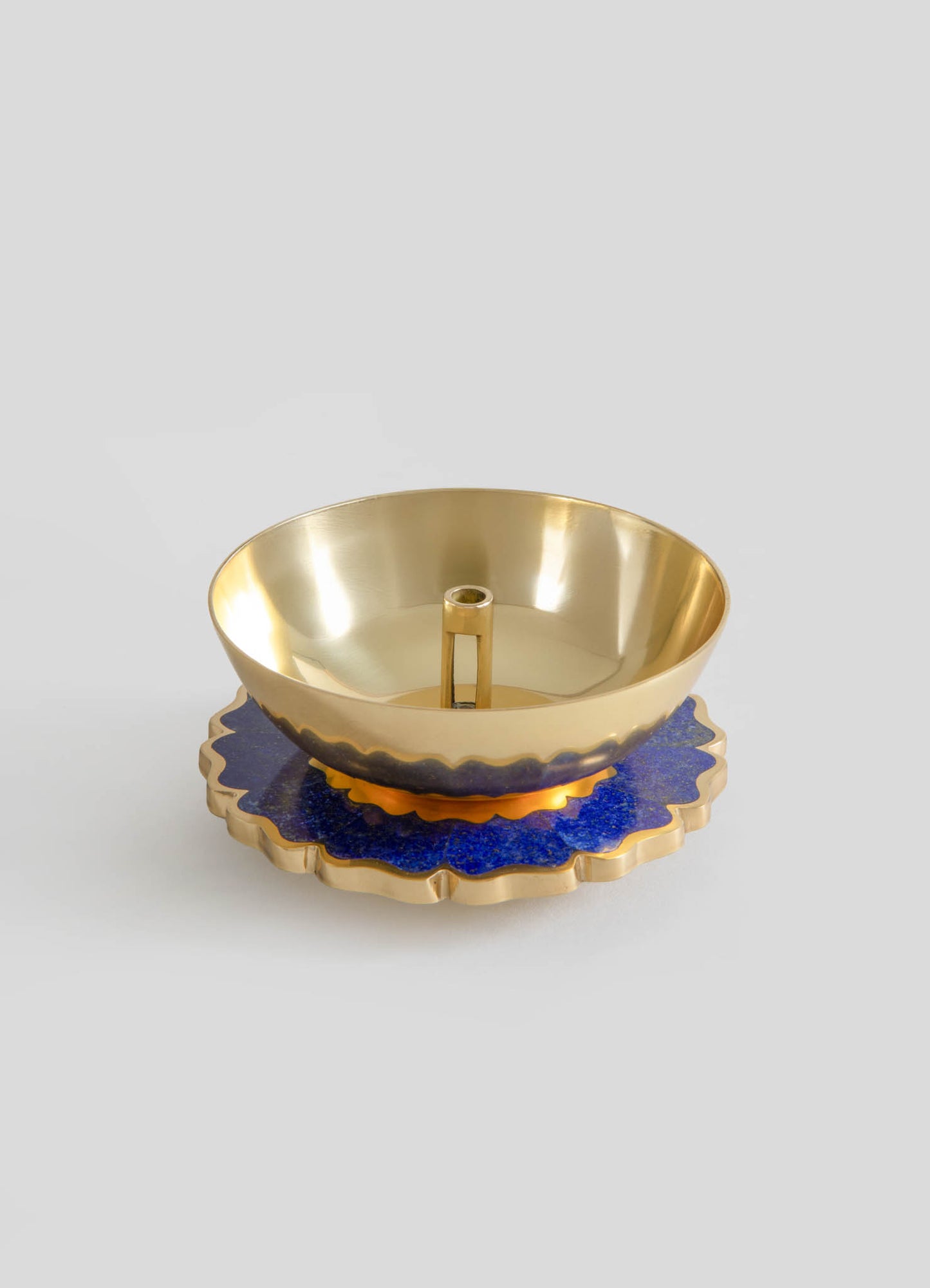 A gold-toned metal bowl with a smooth, reflective surface, placed on a layered blue and gold decorative base with scalloped edges.