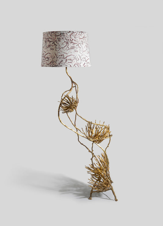 Decorative table lamp with a sculptural brass base resembling twisted branches and a fabric lampshade featuring a floral pattern in neutral tones.