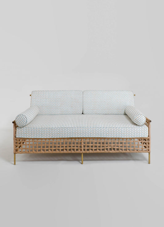 A sofa with a rattan frame, featuring a woven lattice design and supported by slender metal legs, upholstered with a fabric that has a small, repetitive wave pattern in neutral tones. The cushions and bolsters are covered in the same patterned fabric.