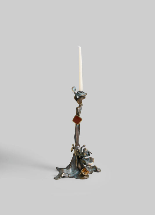 Sculptural candlestick holder with an organic, abstract design in mixed metal tones, featuring irregular shapes and textured surfaces, holding a tall white taper candle.