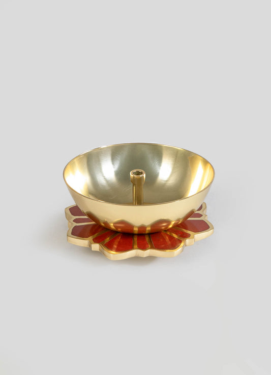 A brass candle holder with a polished gold finish, featuring a central holder for a tealight and a decorative base with a red and gold floral motif.