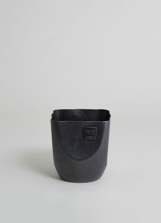 A black ceramic vase with a matte finish, featuring an irregular rounded shape and a small square handle on the side. The vase has a contemporary style with minimalist design and smooth, organic lines.