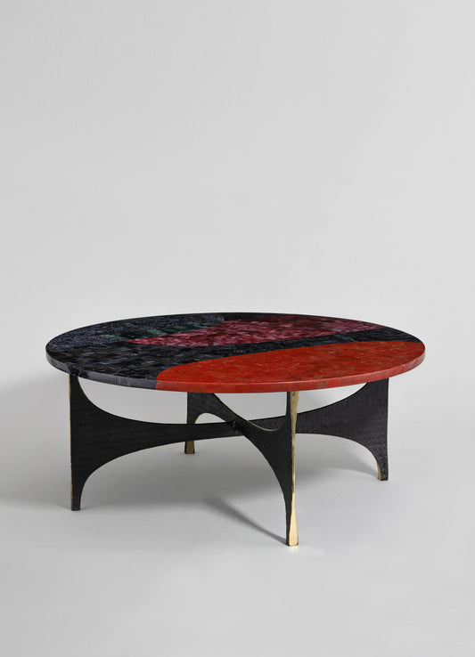 A round coffee table with a mosaic-style glass top featuring red, black, and green tones, resting on a black and gold-finished wooden base with curved supports.