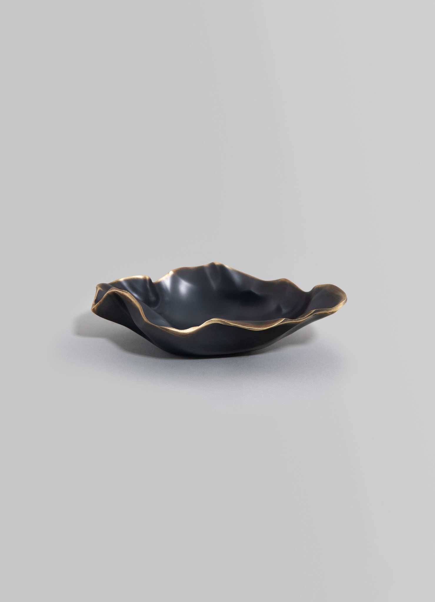 Black ceramic bowl with an irregular, wavy edge and metallic gold accents, featuring a handcrafted design.