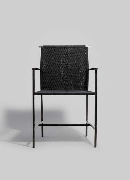 A modern lounge chair with a black woven textile backrest featuring a geometric chevron pattern, supported by a sleek black metal frame. The design emphasizes contemporary style and minimalist aesthetics.