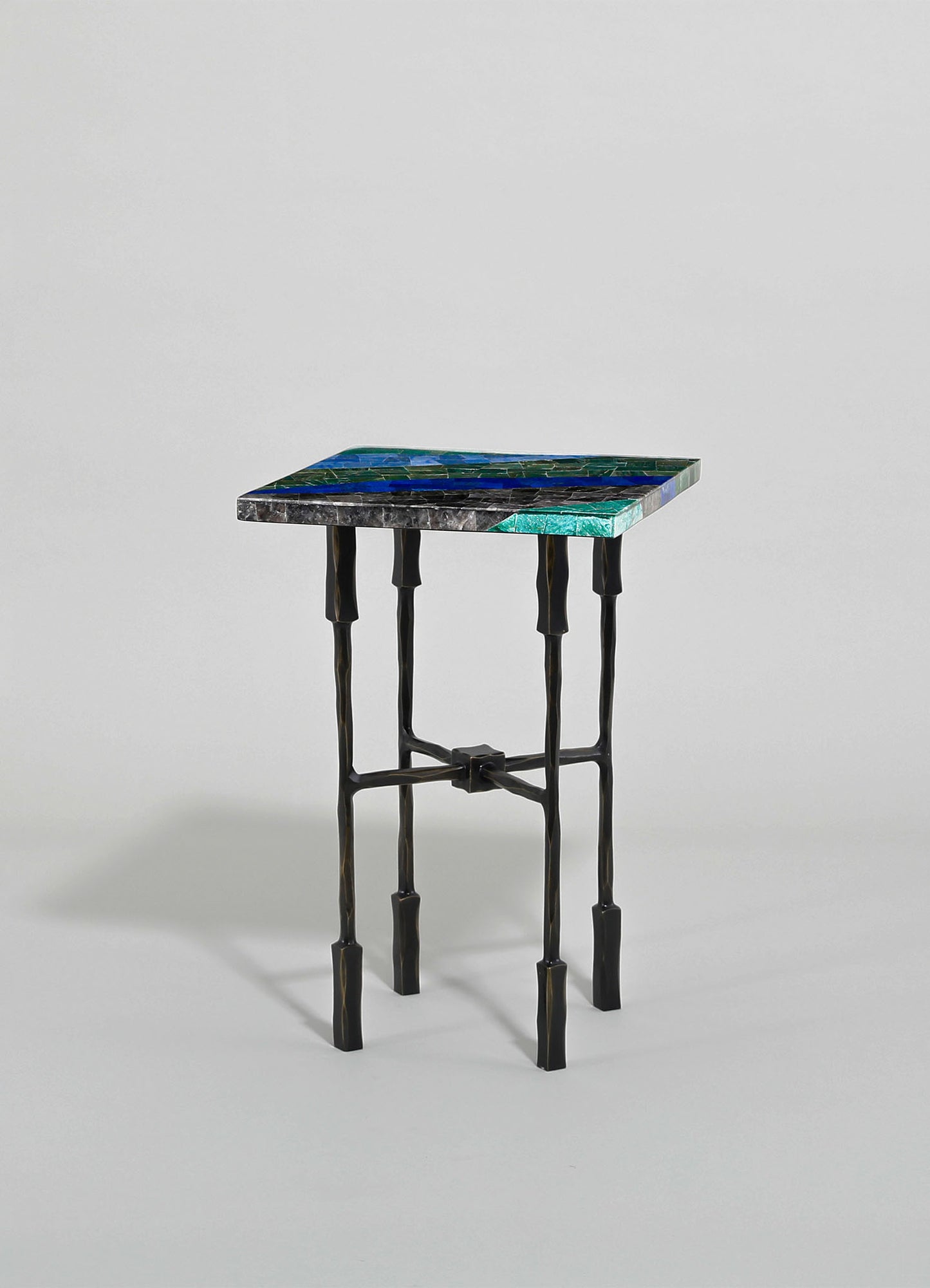 A side table with a mosaic tiled top featuring shades of blue, green, and black, and a black metal frame with a sculptural, irregular design.