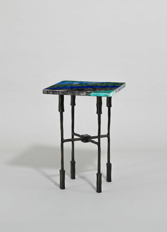 A side table with a mosaic tiled top featuring shades of blue, green, and black, and a black metal frame with a sculptural, irregular design.