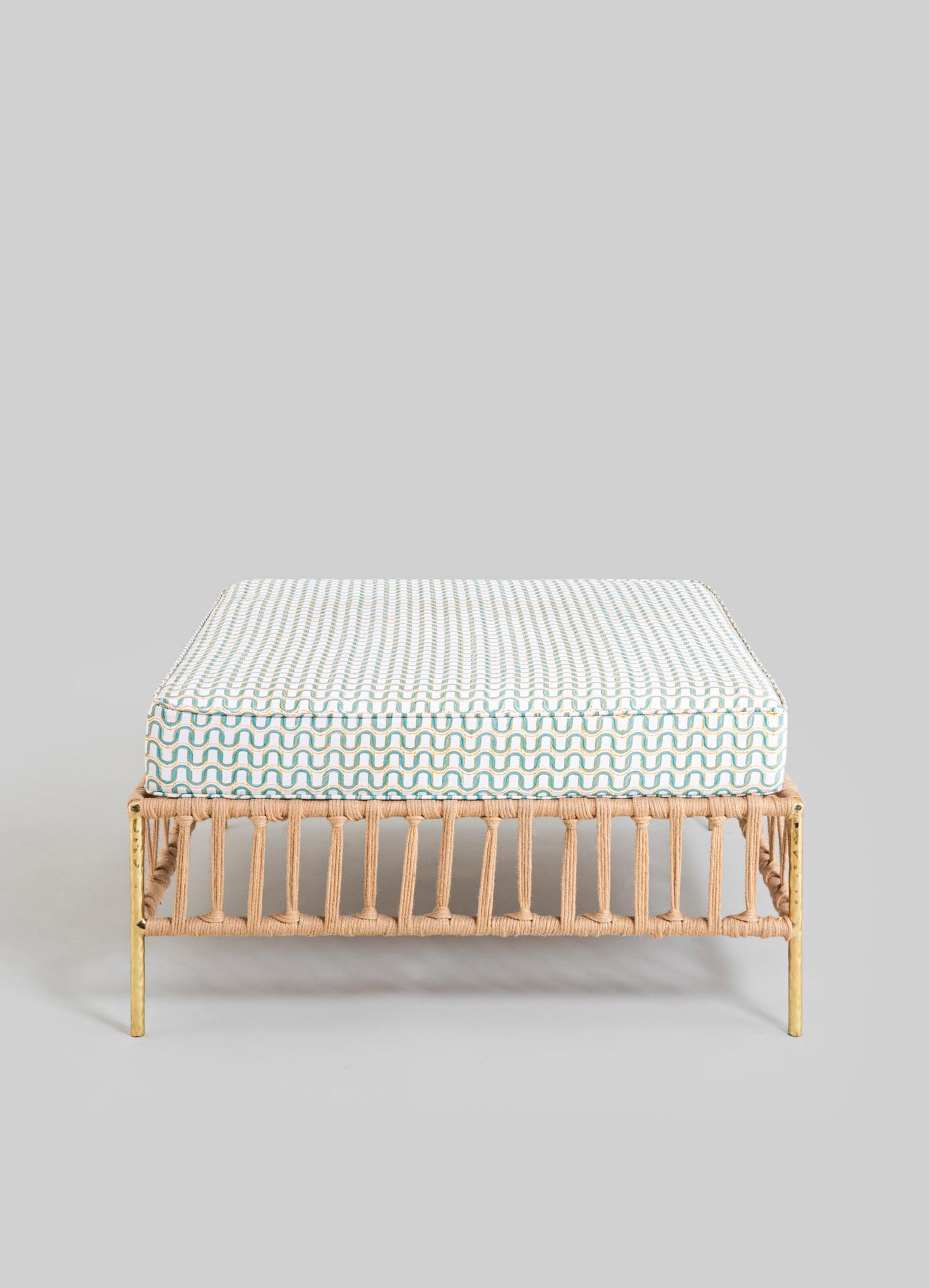 A rectangular upholstered cushion with a geometric pattern featuring wavy lines in shades of beige, light blue, and white, placed on a rattan bench with a natural finish and vertical slats.