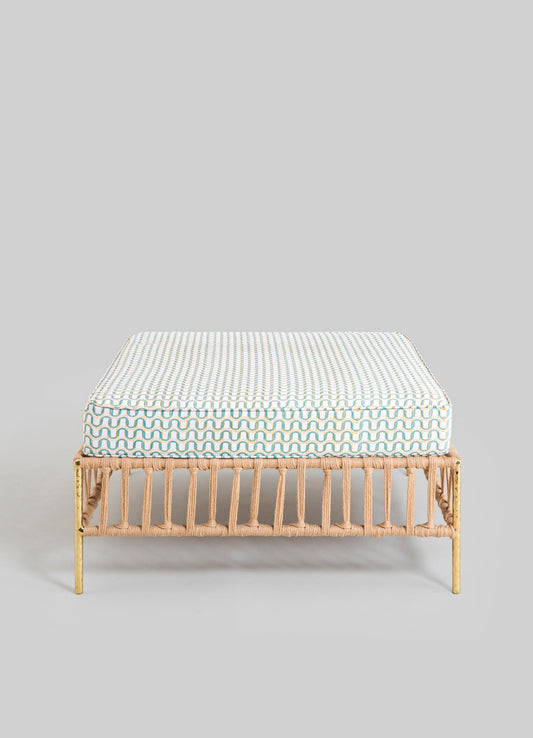 A rectangular upholstered cushion with a geometric pattern featuring wavy lines in shades of beige, light blue, and white, placed on a rattan bench with a natural finish and vertical slats.