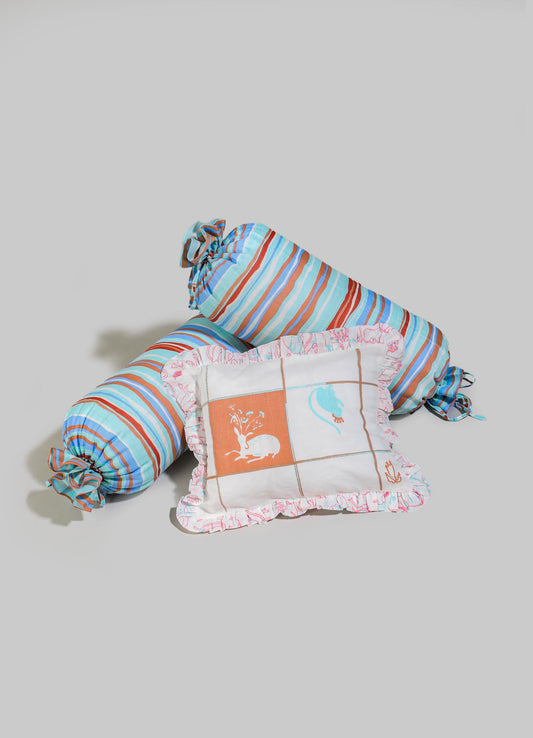 Striped fabric cushions and bolster pillow made of soft cotton with colorful patterns in shades of blue, orange, and white. The items feature ruffled edges and tie closures, with motifs including a tree, a bird, and abstract designs, evoking a handcrafted, whimsical style.