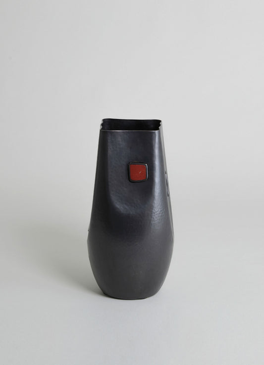 A black metal vase with a hammered texture, featuring a rectangular red accent on the front and a smooth, rounded form. The design is contemporary with minimalistic style.